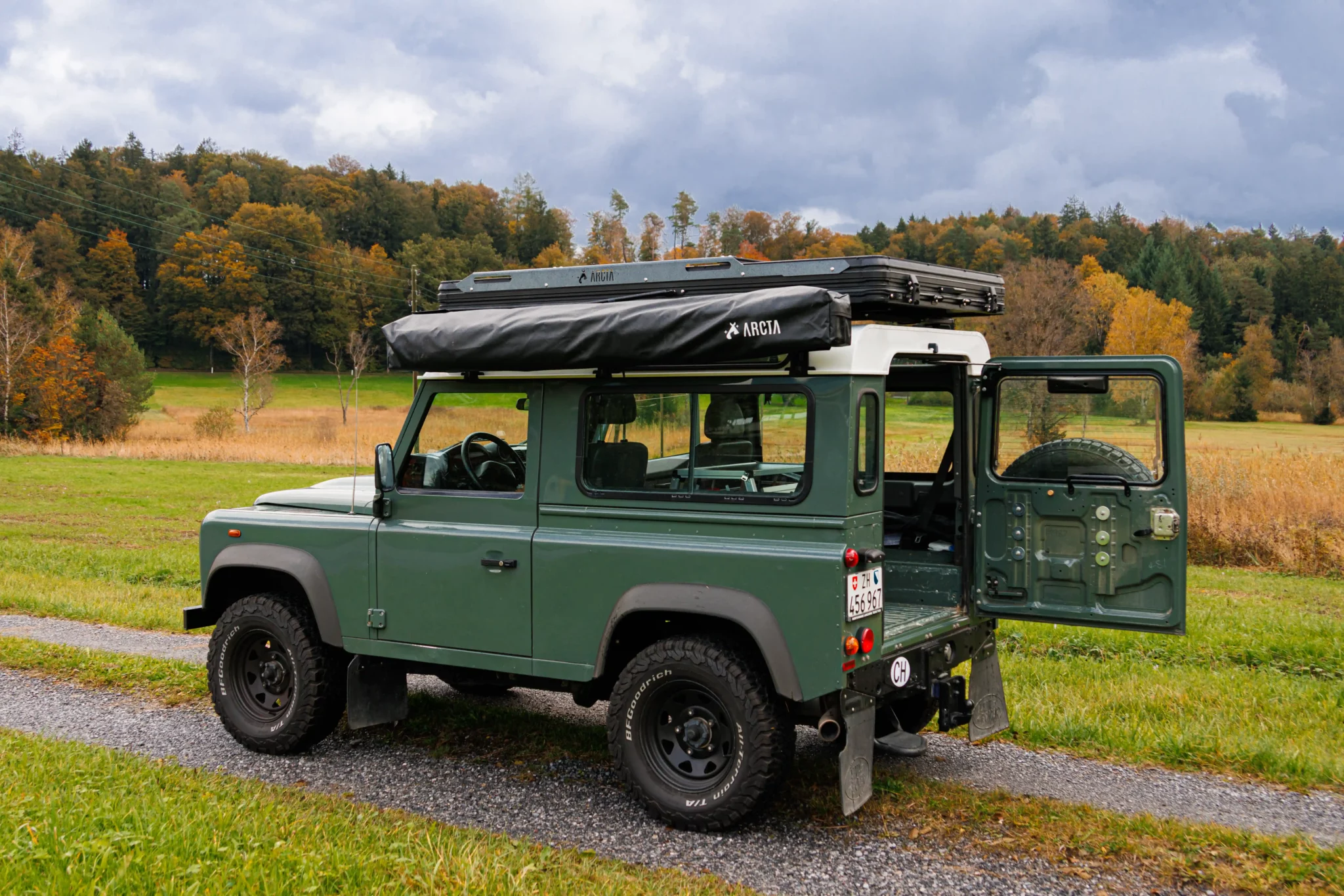 Land Rover Defender 90 mit geschlossenem Dachzelt und Markise auf einer Landstrasse im Herbst