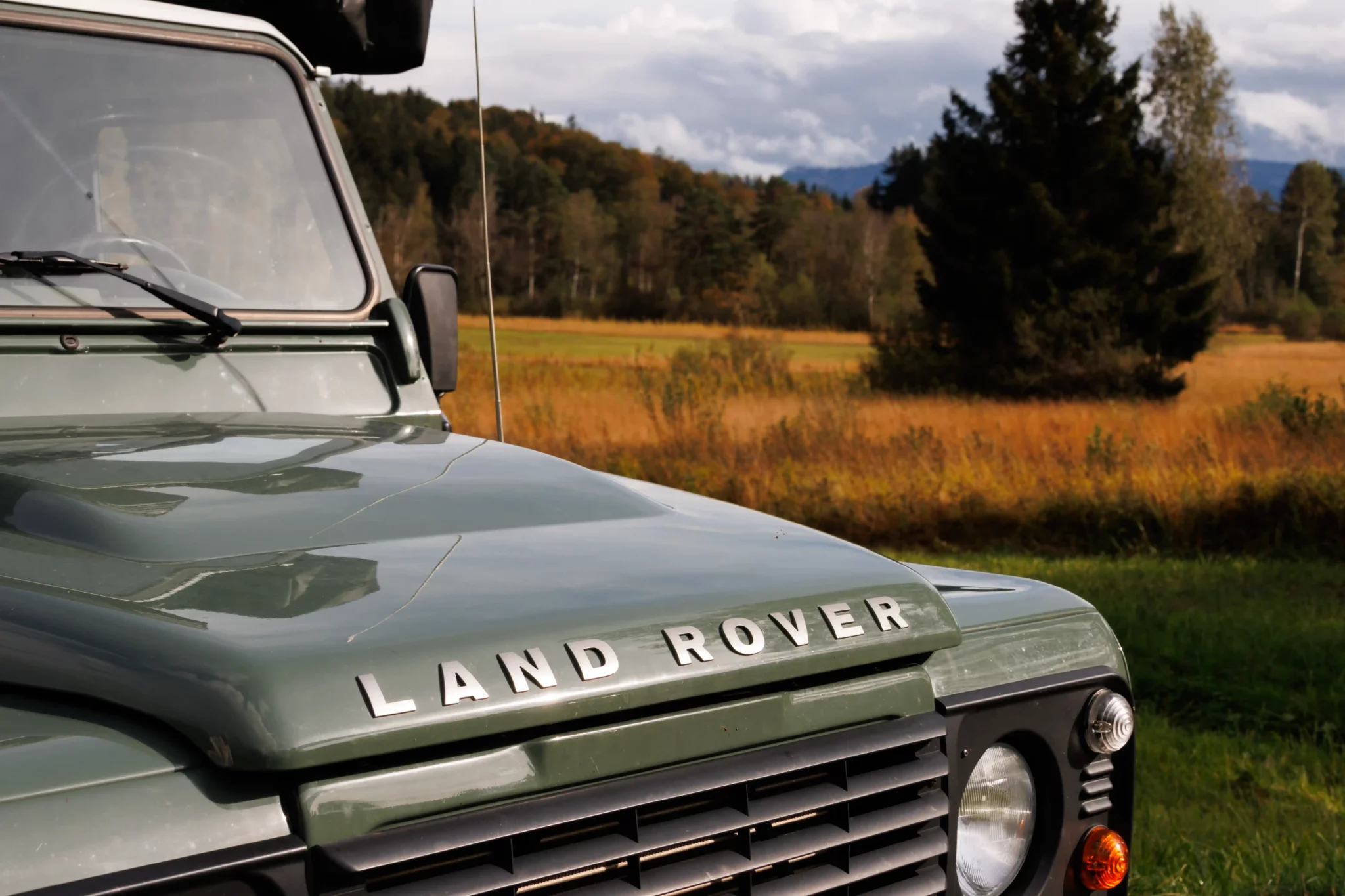 Front des Land Rover Defender im Keswick Green, Herbstlandschaft im Hintergrund